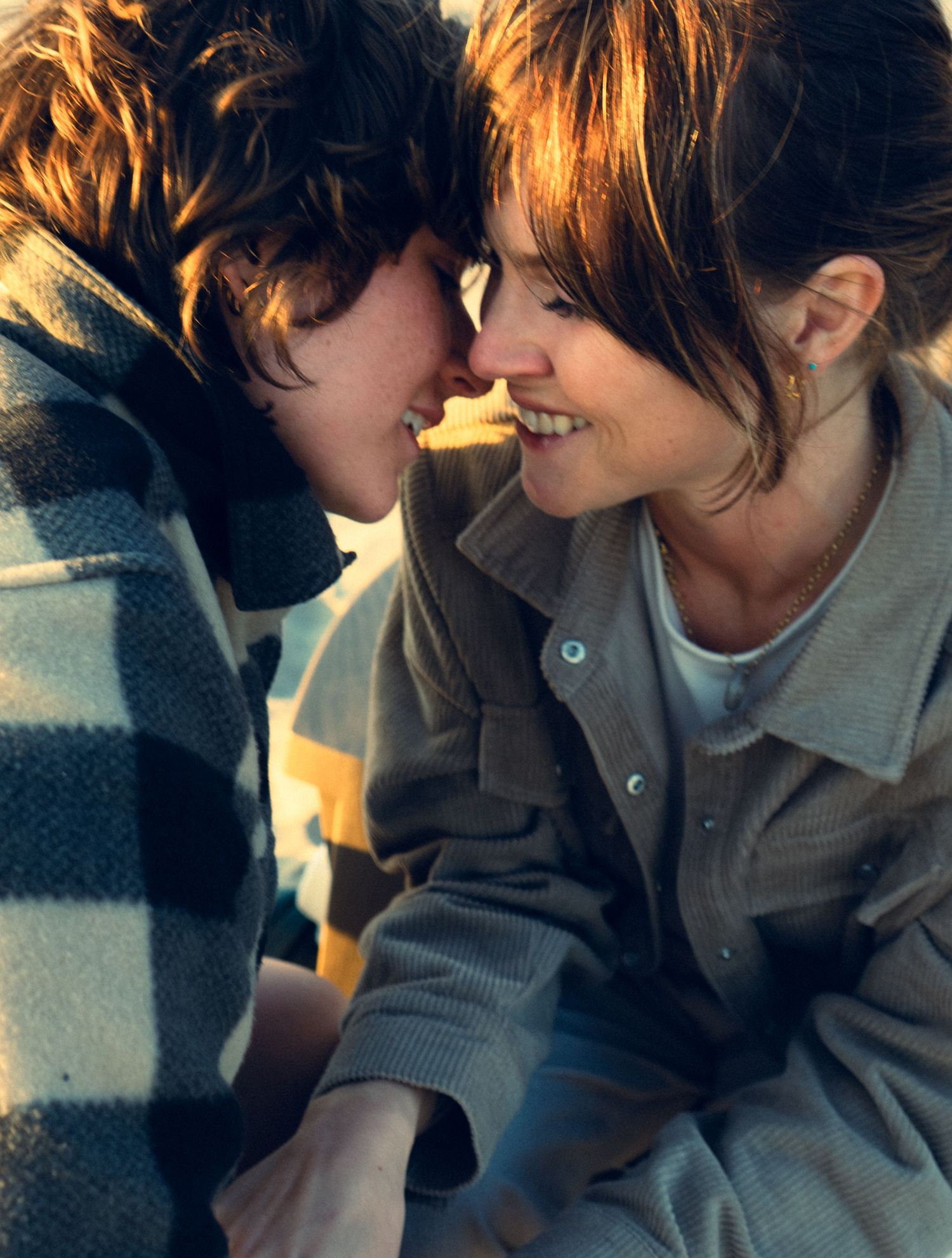 Young couple touching foreheads and smiling warmly while wrapped in a plaid blanket outdoors.
