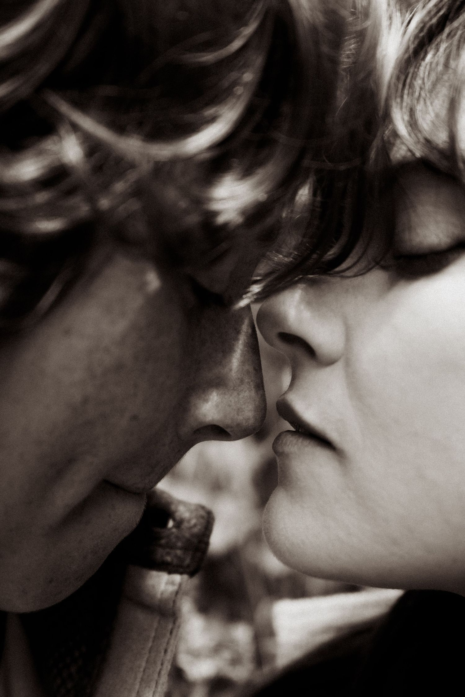Black and white close-up of a couple about to share a tender kiss in soft natural lighting.