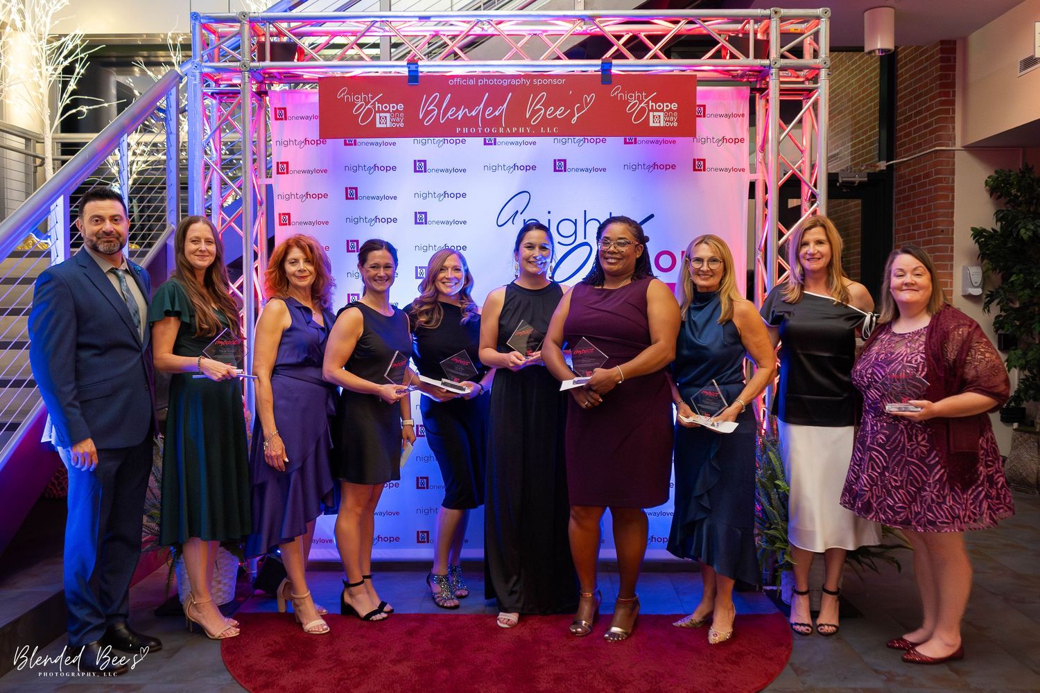 Group of award recipients posing with trophies in front of a branded step-and-repeat backdrop at a gala.