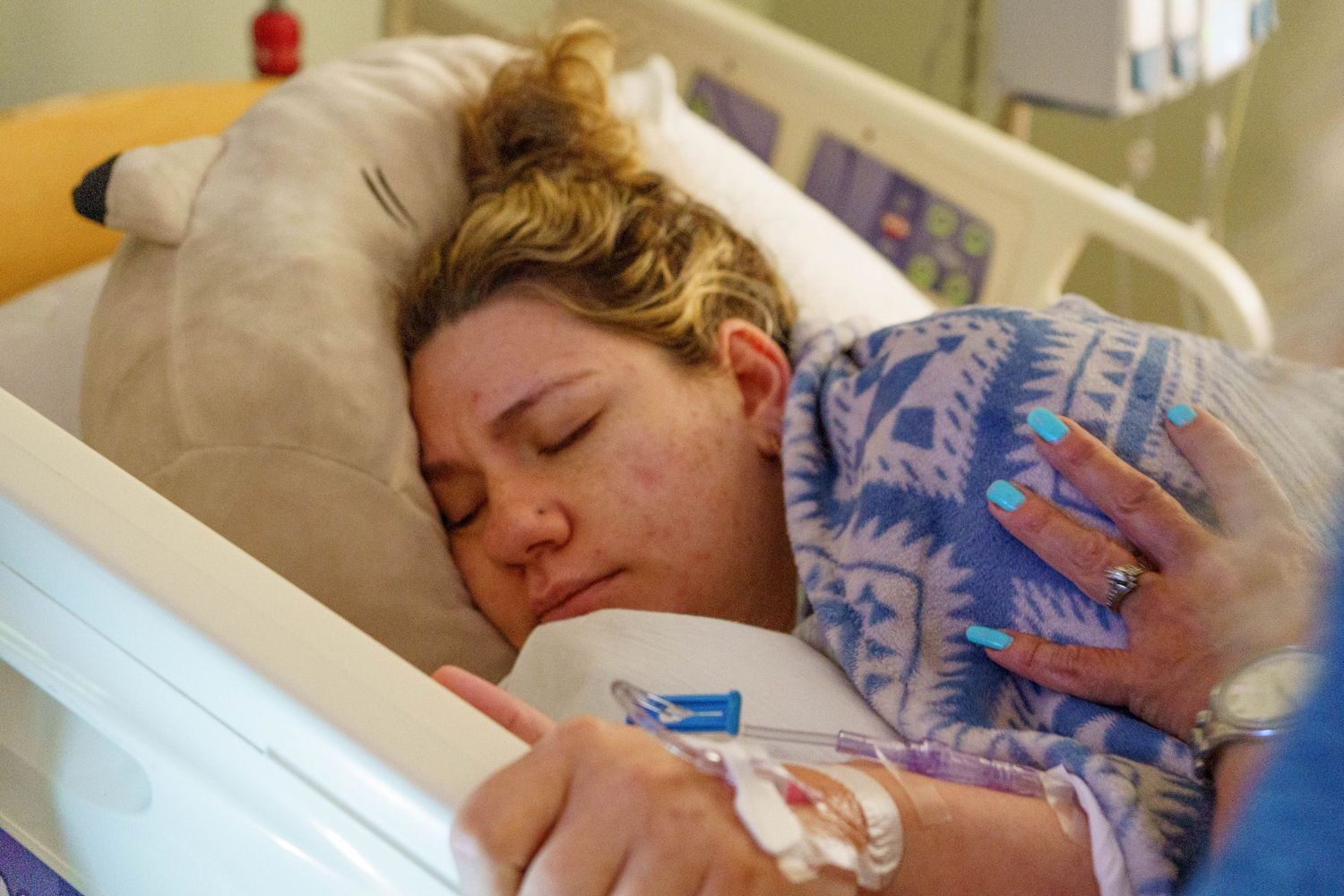 New mother resting in hospital bed while cradling her newborn baby after delivery.