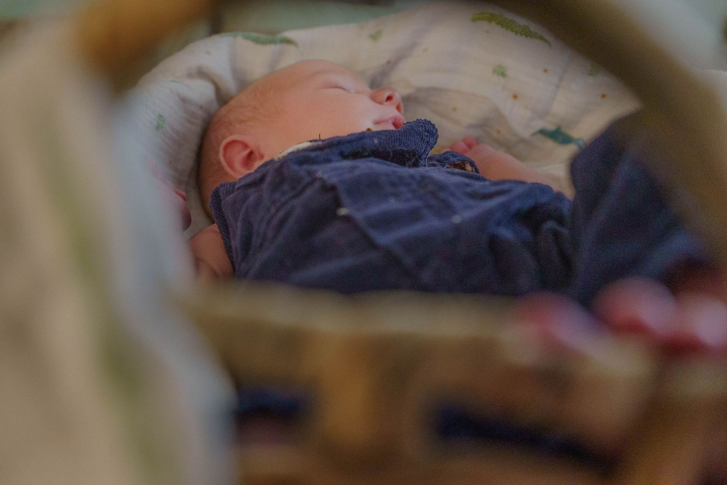 Sleeping newborn baby wrapped in blue blanket resting in a wicker bassinet.