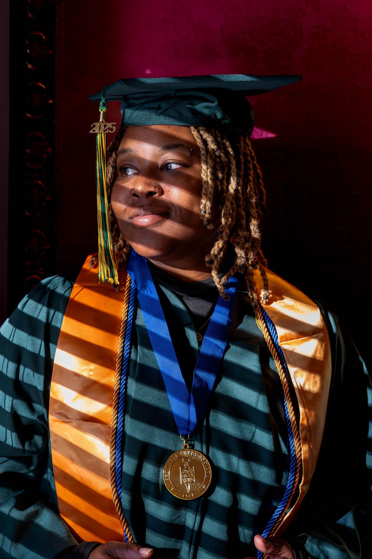 Graduate wearing cap, gown, and gold medal poses proudly in dramatic lighting for class of 2025.