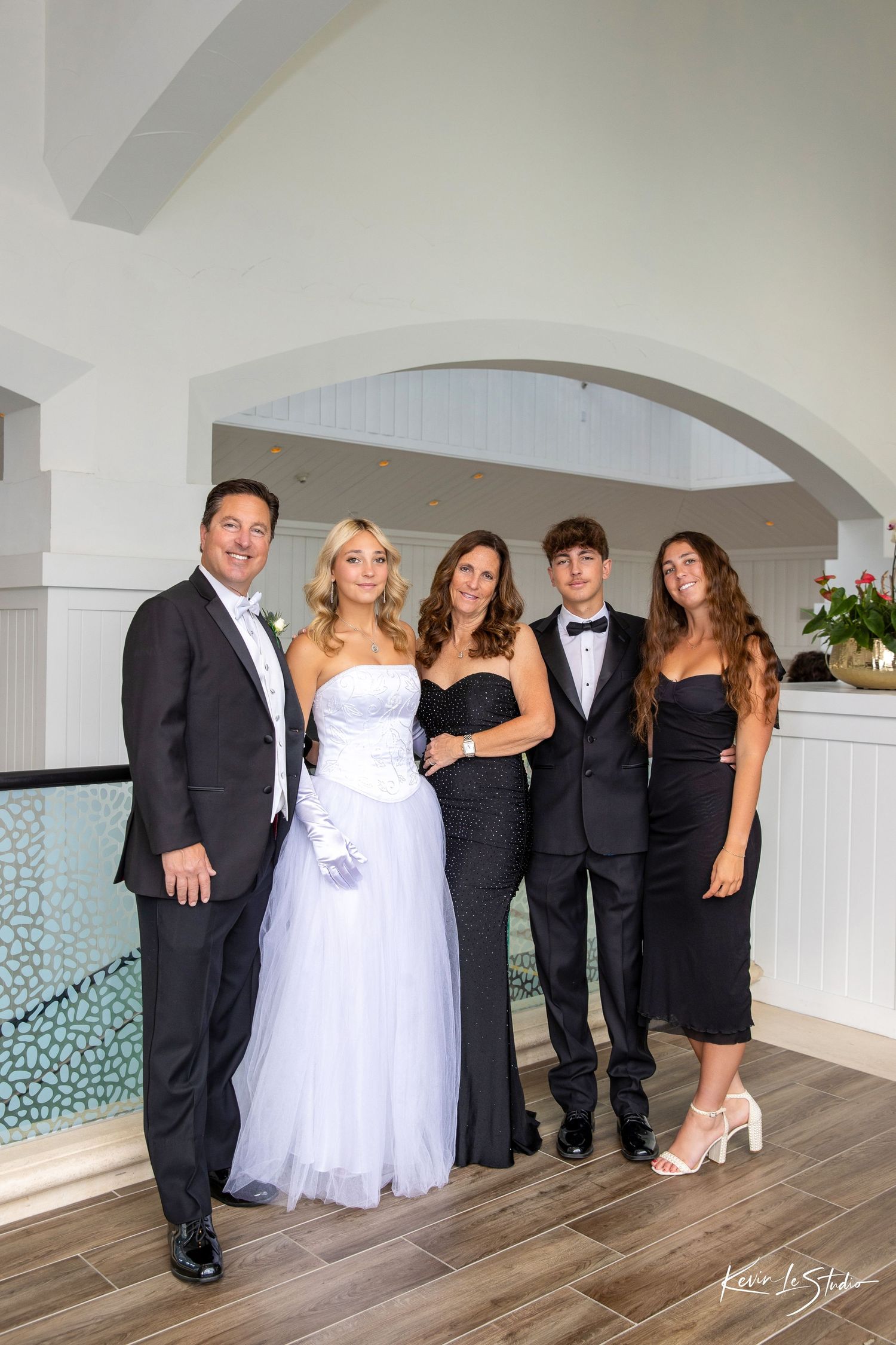 Family of five posing elegantly in formal attire, including a girl in a white ball gown, at a special occasion venue.