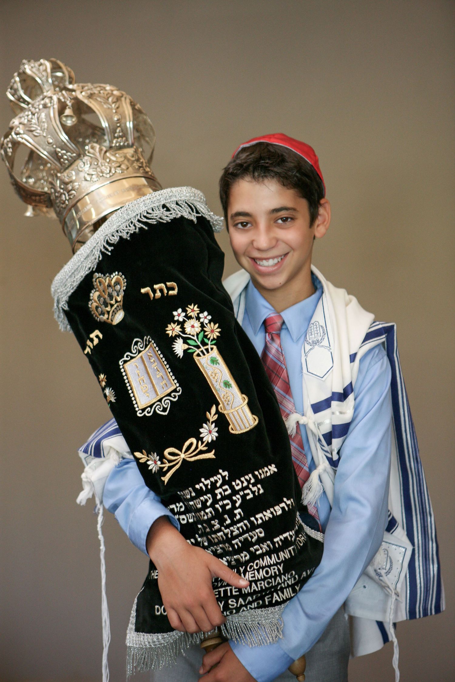 Smiling boy in tallit holding Torah scroll at his Bar Mitzvah ceremony.