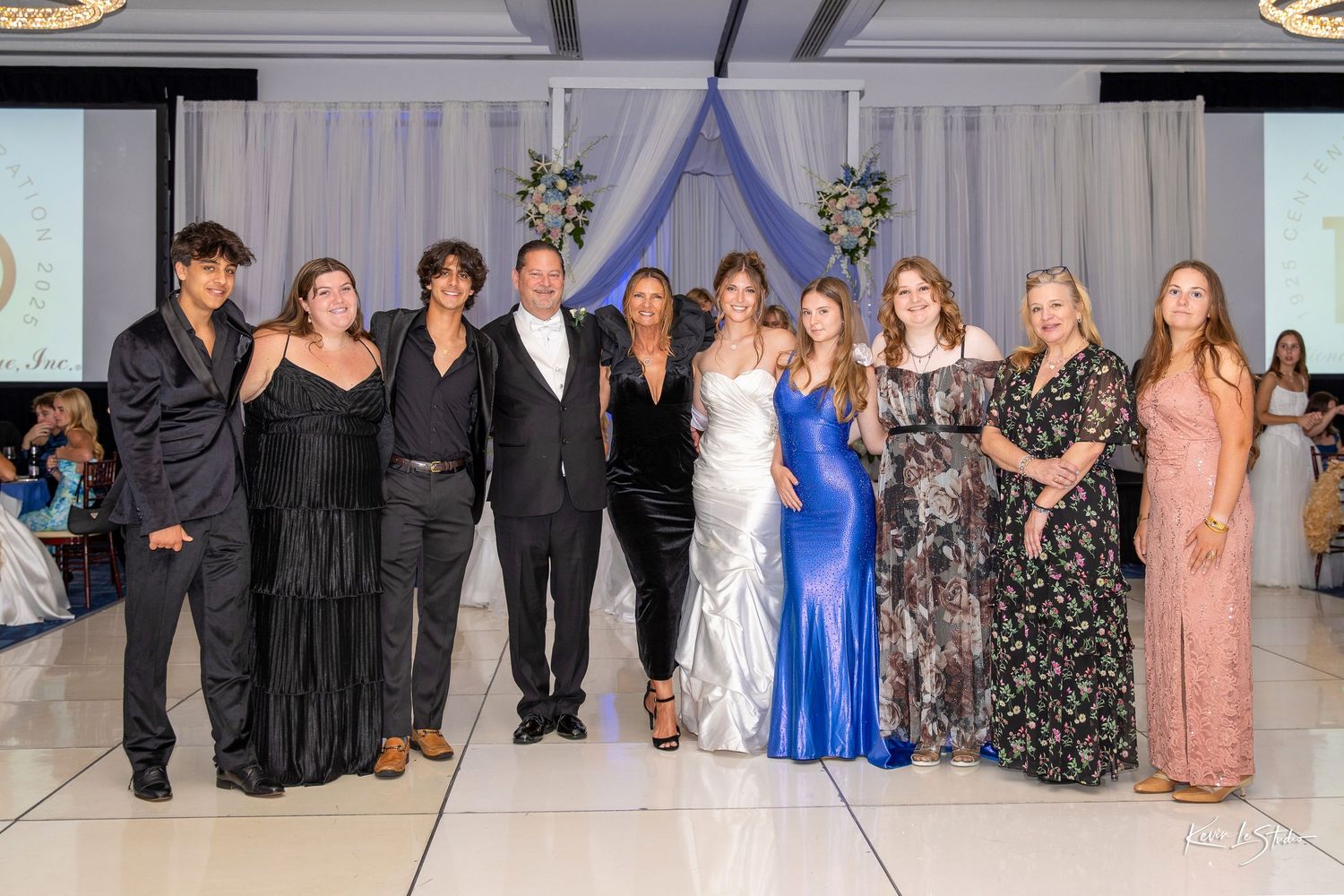 Group of elegantly dressed people posing together on a runway at a formal fashion show event.