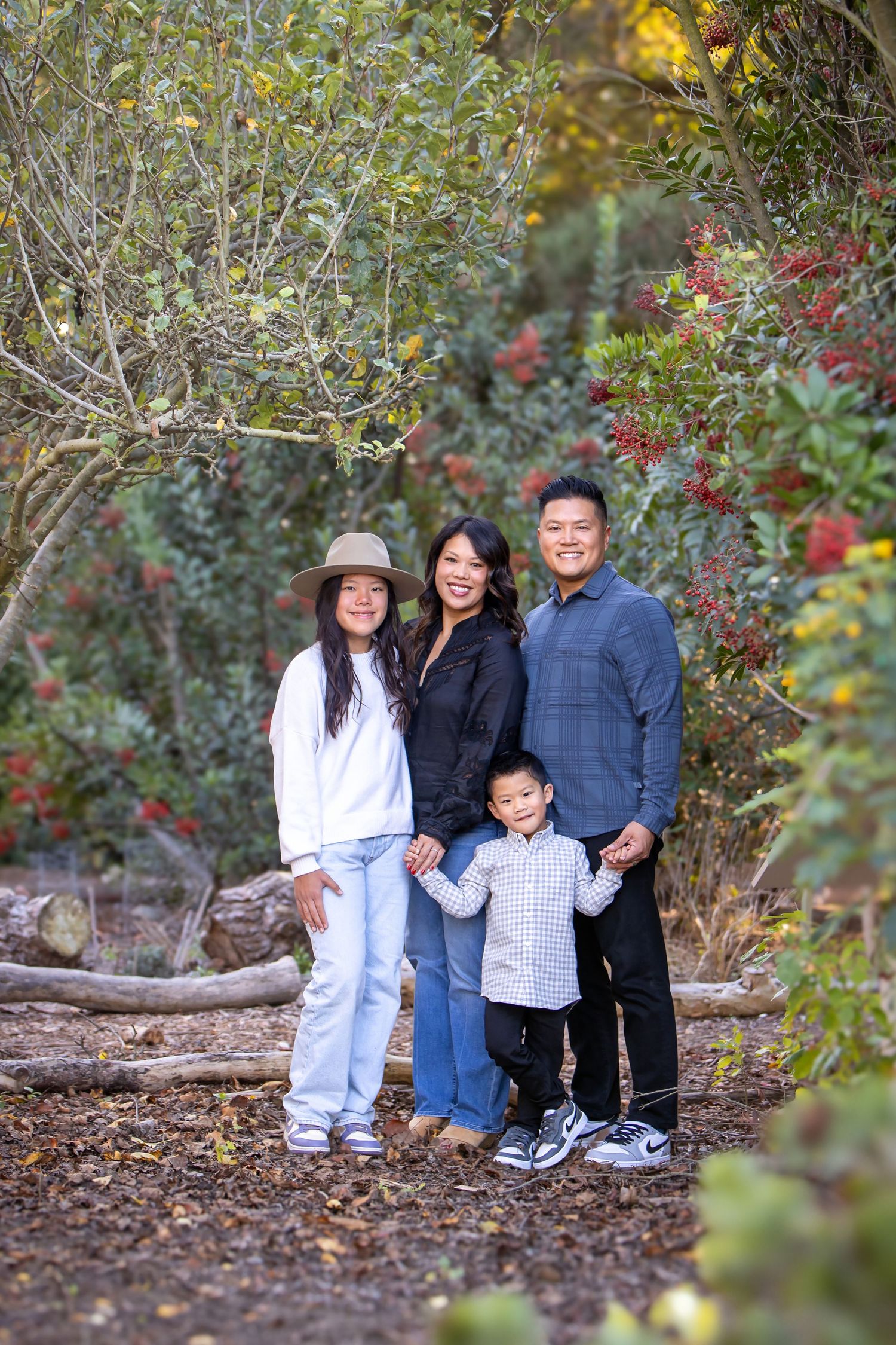 Family of four posing outdoors among lush greenery and red berries, smiling together on a nature trail.