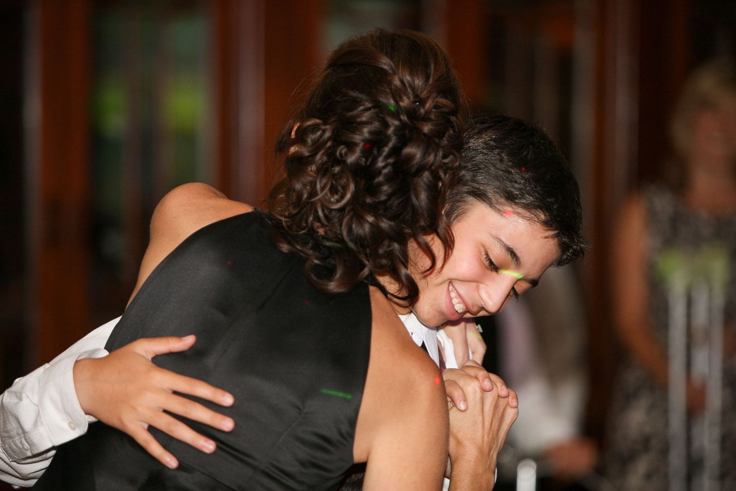 Two people sharing a warm embrace and smiling at a formal event, possibly a wedding reception.