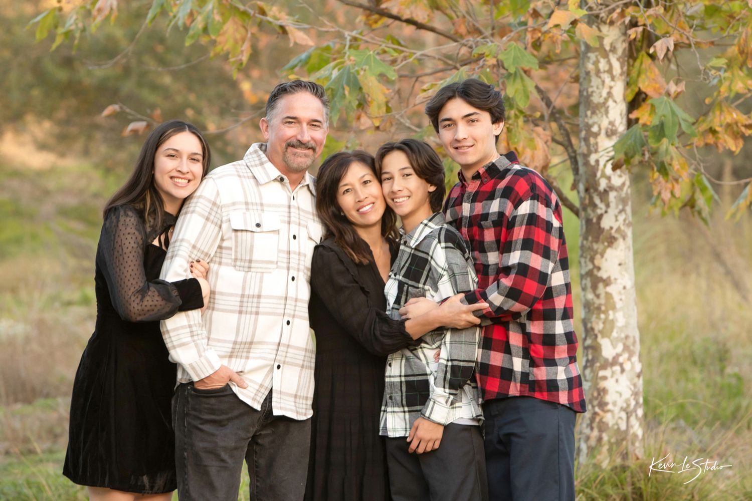 Family of five smiles together outdoors near a tree in a warm autumn portrait session.