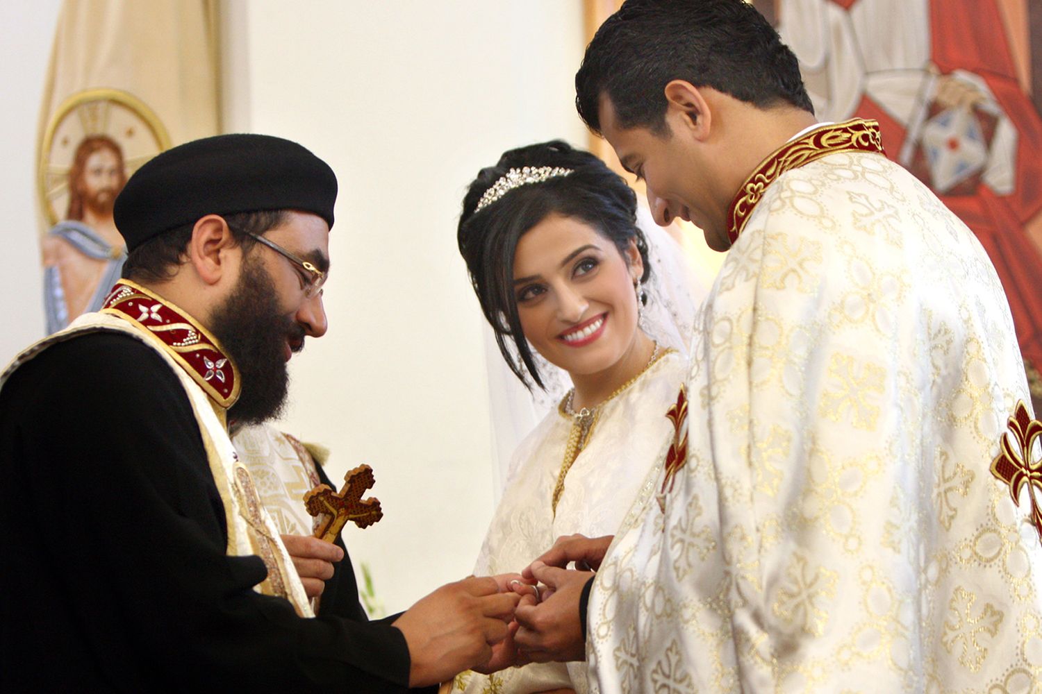 Priest places wedding rings on couple during a traditional Coptic Orthodox Christian wedding ceremony in church.