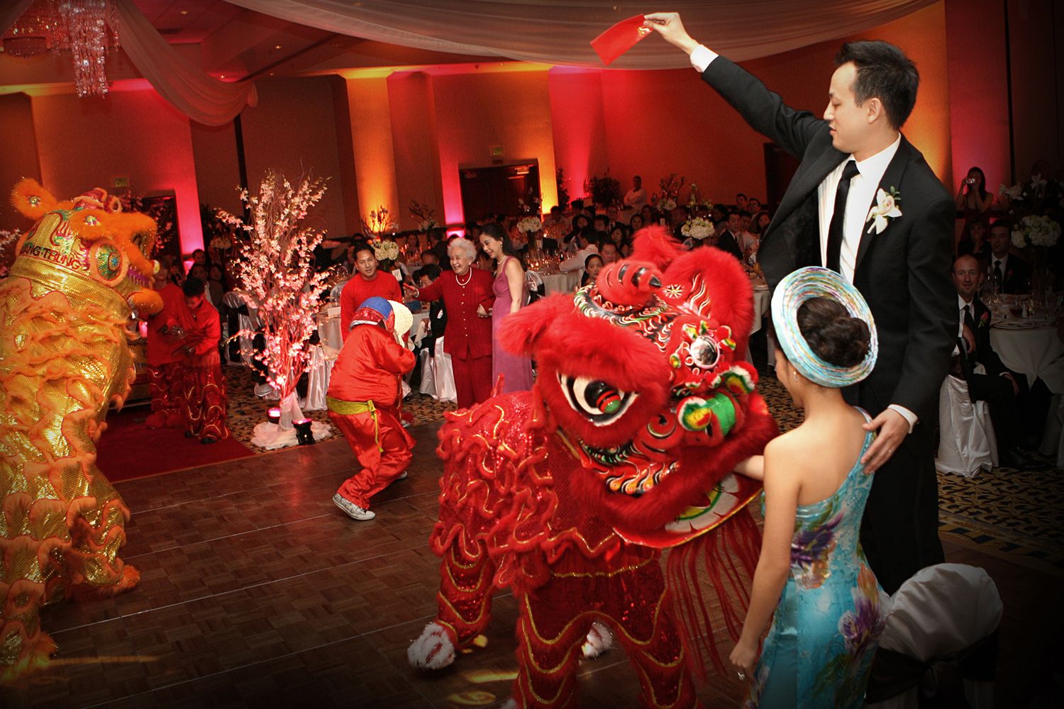 Chinese lion dance performance at vibrant wedding reception with red decorations.