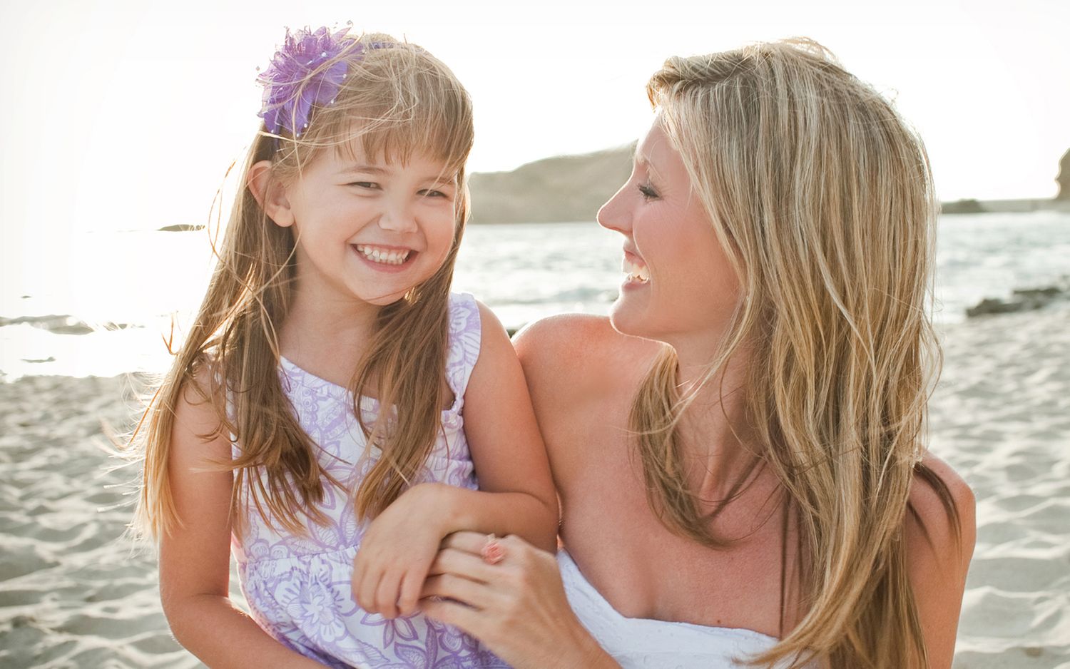 Happy mother and daughter smiling together on a sunny beach.