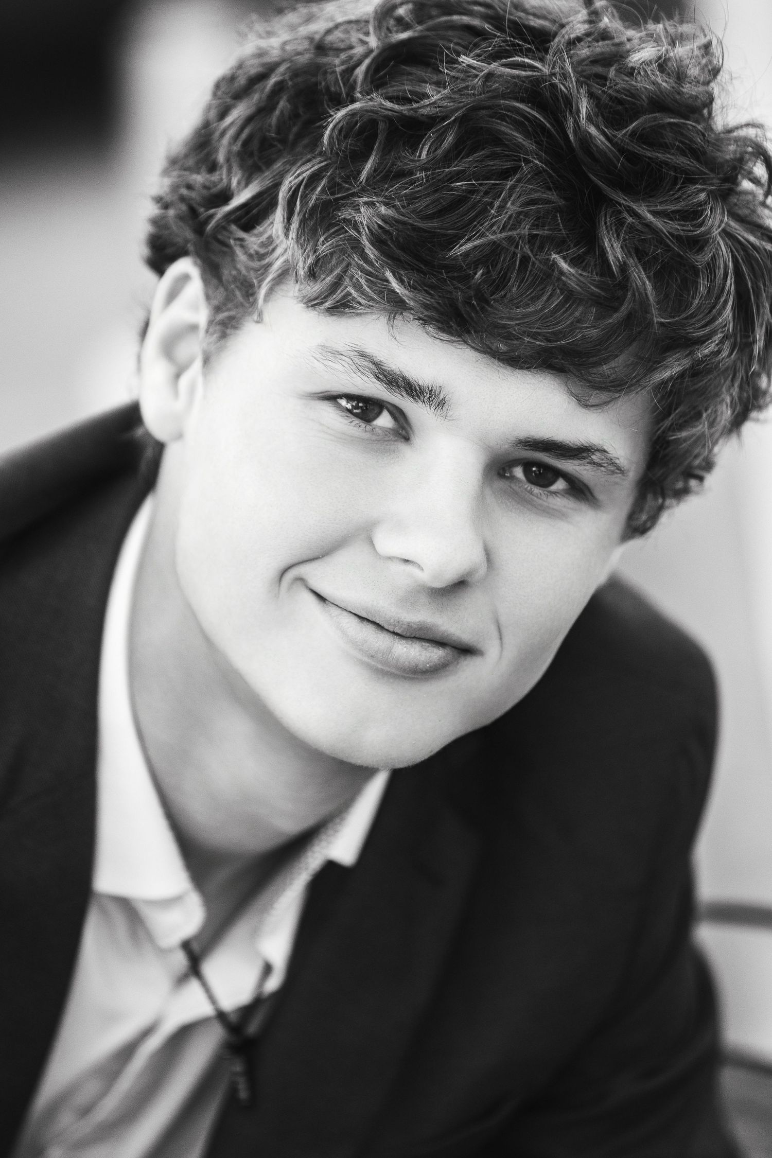 Black and white portrait of a smiling young man with curly hair wearing a blazer.