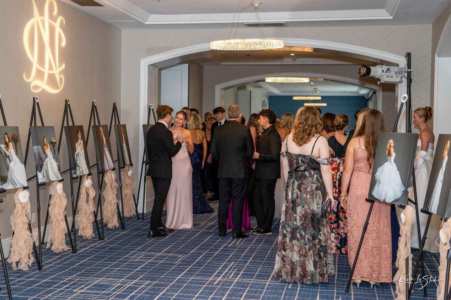 Elegantly dressed guests mingle in a formal event hall lined with framed artwork displays at a gala.