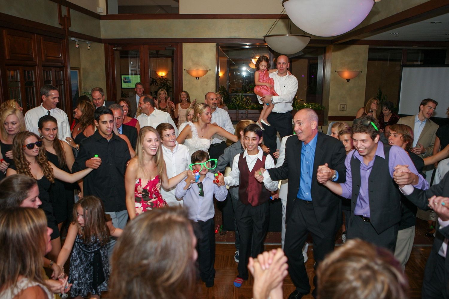 Guests celebrate on the dance floor at a lively indoor wedding reception with the bride and groom.