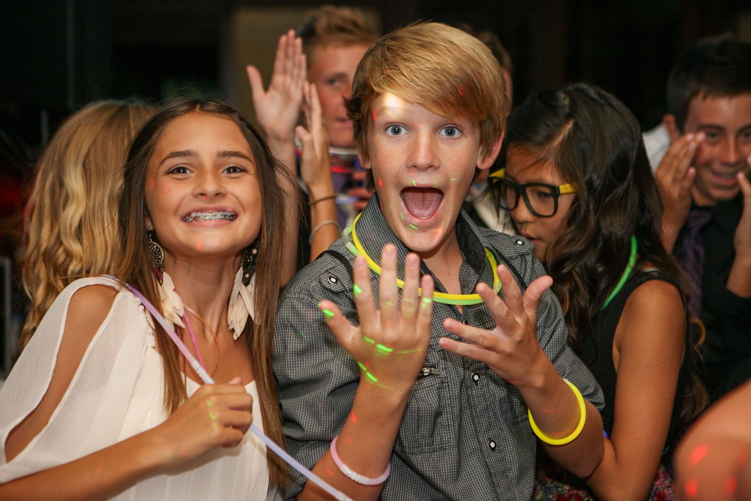 Excited kids at a party with glow bracelets, boy showing hands, girl smiling, colorful event atmosphere.