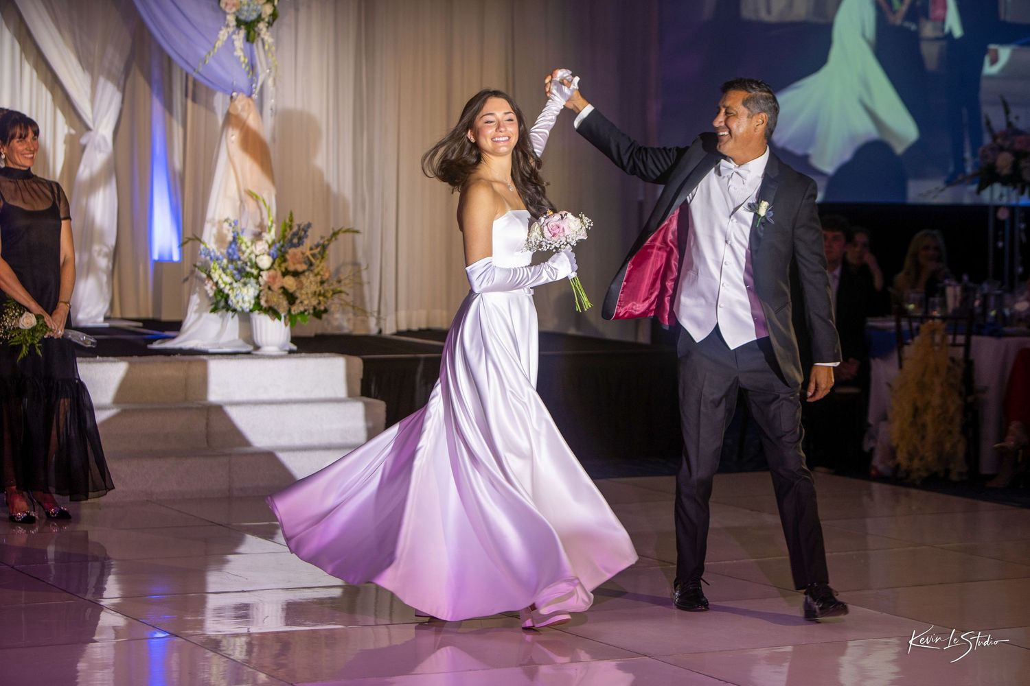 Bride and groom share first dance at elegant wedding reception, bride twirling in white gown under sparkling lights.