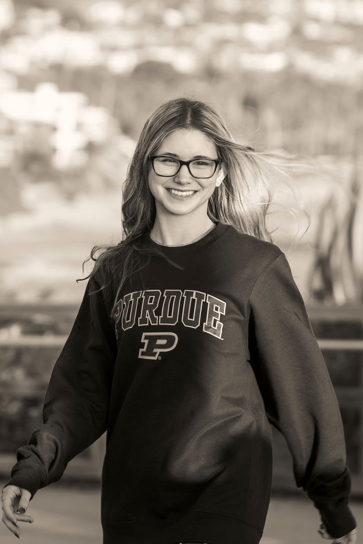Black and white photo of smiling girl in Purdue sweatshirt with wind-blown hair outdoors.