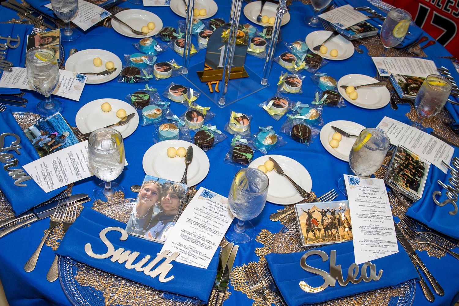 Elegant blue tablecloth event setup with name placards, decorative centerpieces, plates, and glassware for a formal banquet.