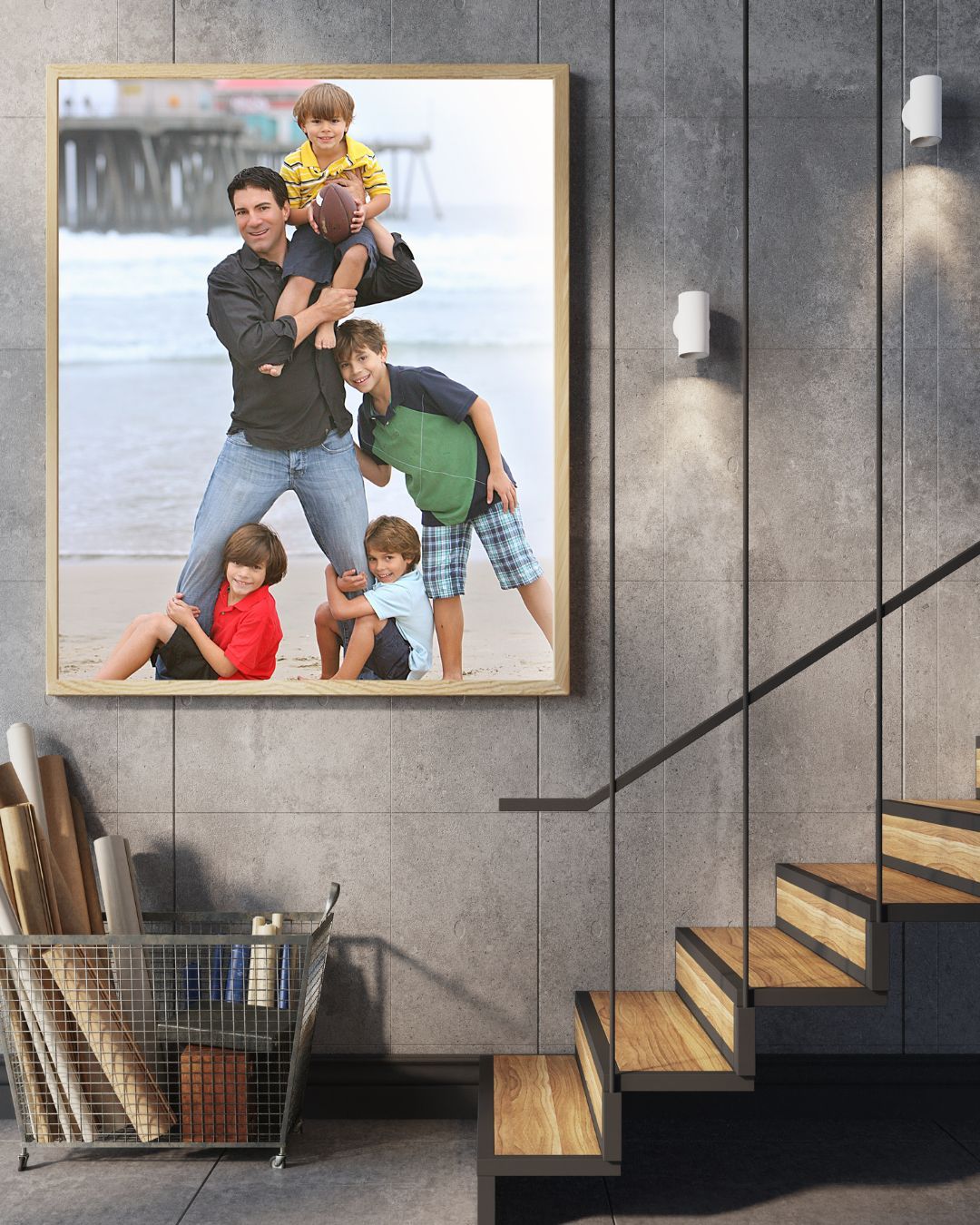 A framed family beach photo displayed on a concrete wall above stairs, showing a father with four children playing with a football.