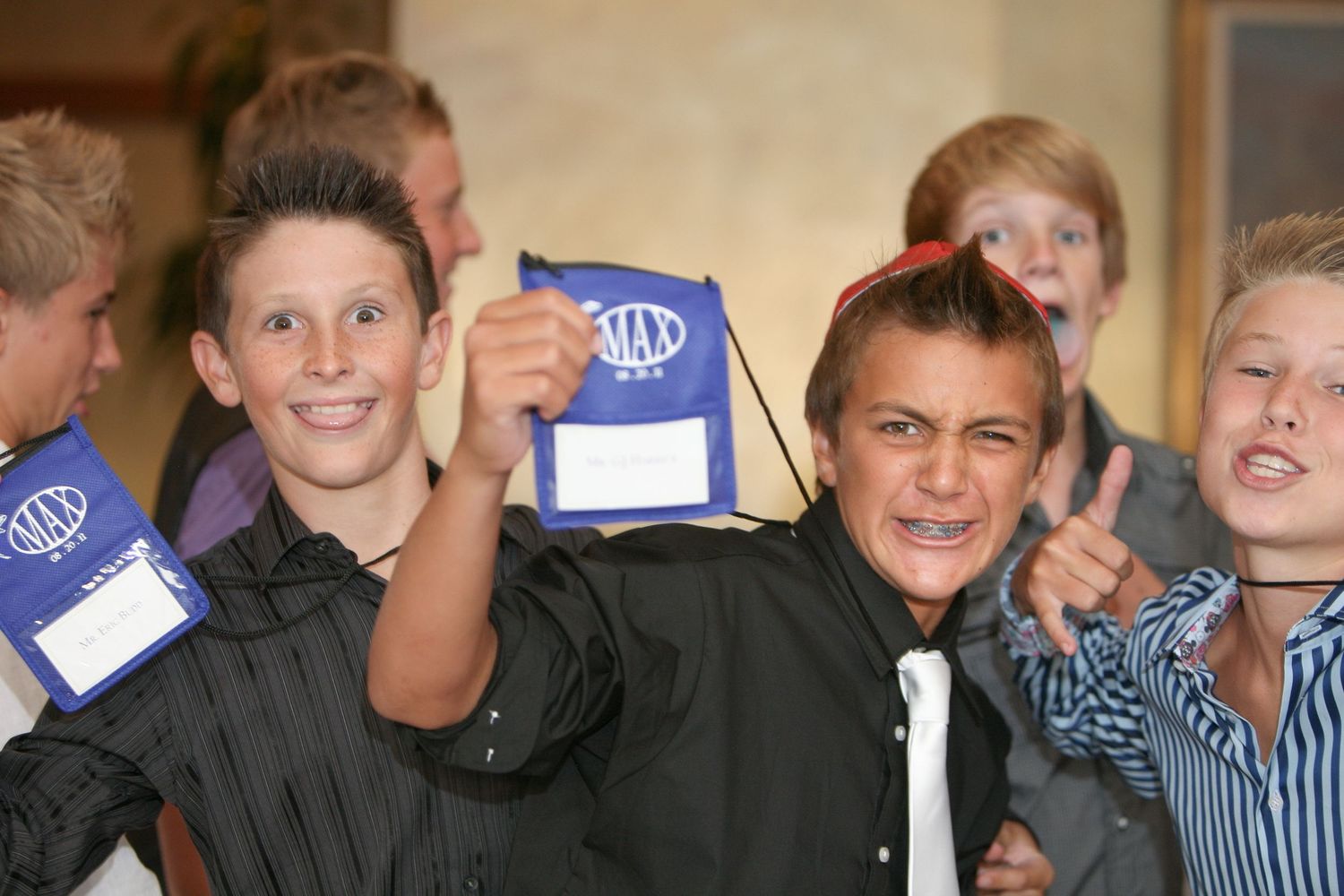Excited young boys holding blue MAX branded bags at an event, smiling and pointing at the camera.