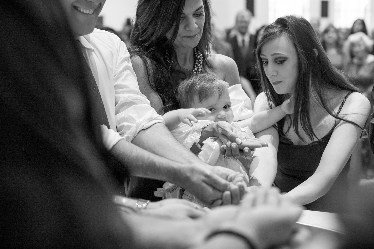 Black and white photo of family gathered around a baby during a christening ceremony in a church.