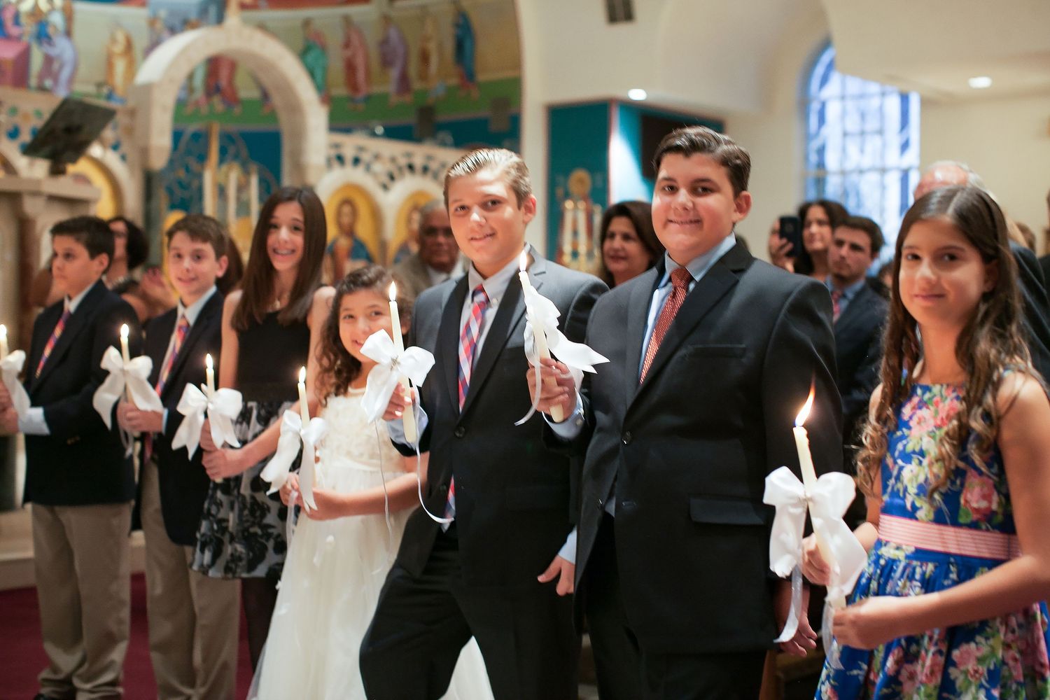 Group of children and adults in formal attire holding white doves and candles during a church ceremony.
