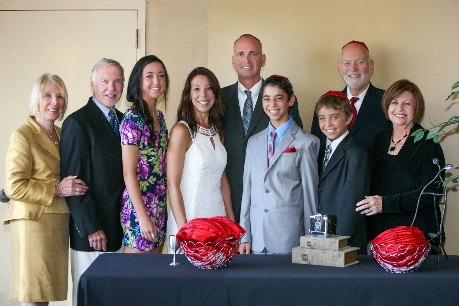 Family group photo at a formal celebration, posing together with decorative red centerpieces on a table.