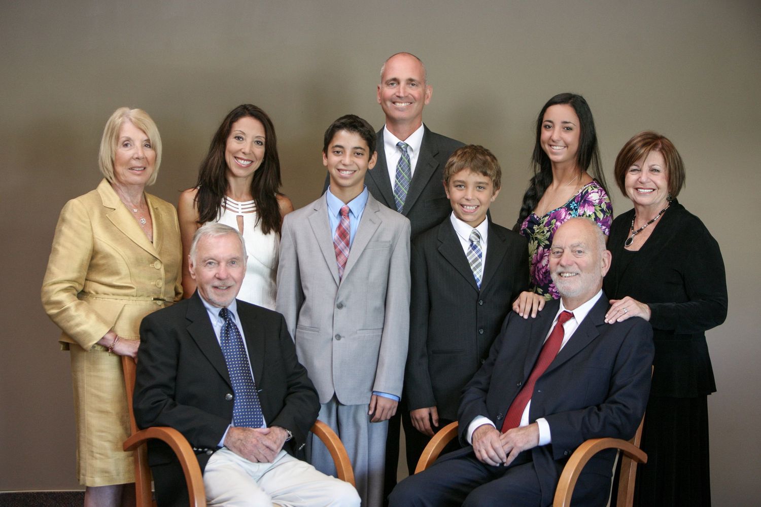 Family portrait of nine people, two seated elders and seven standing adults and teens, dressed in formal attire.