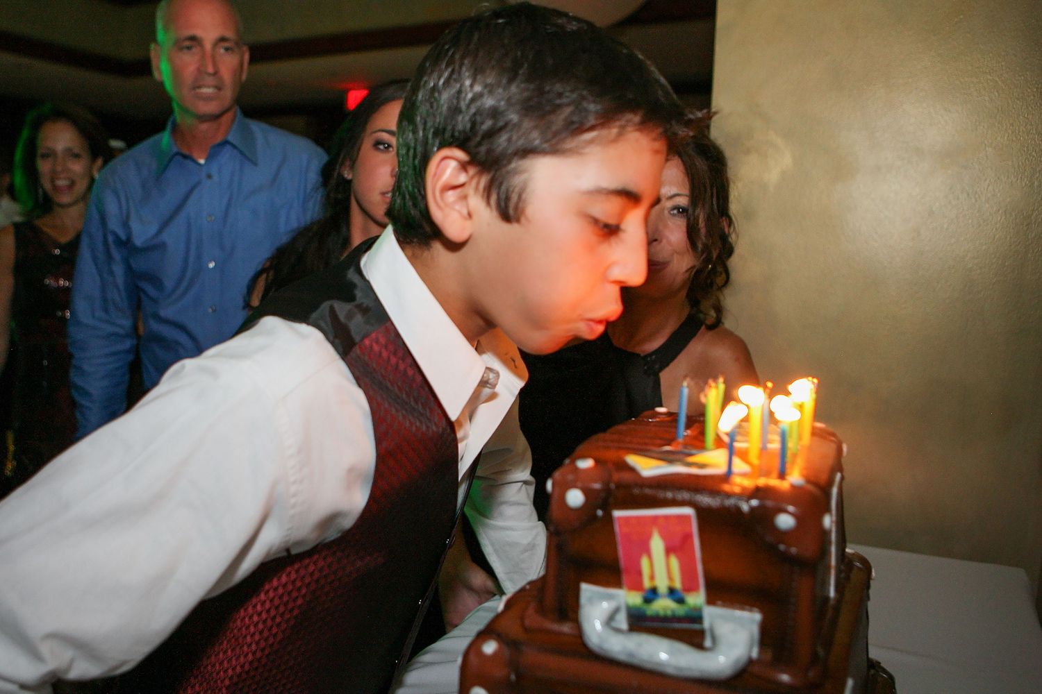 Boy blowing out candles on a chocolate birthday cake at a party celebration.