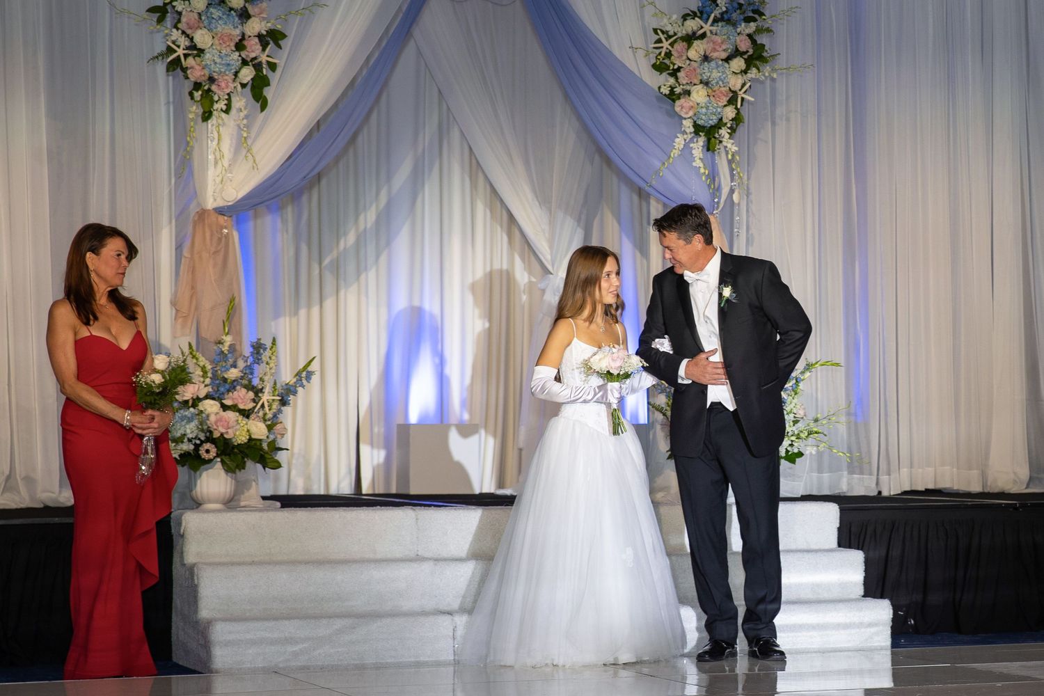Bride and groom exchange vows at elegant wedding ceremony with white drapes and floral arrangements.