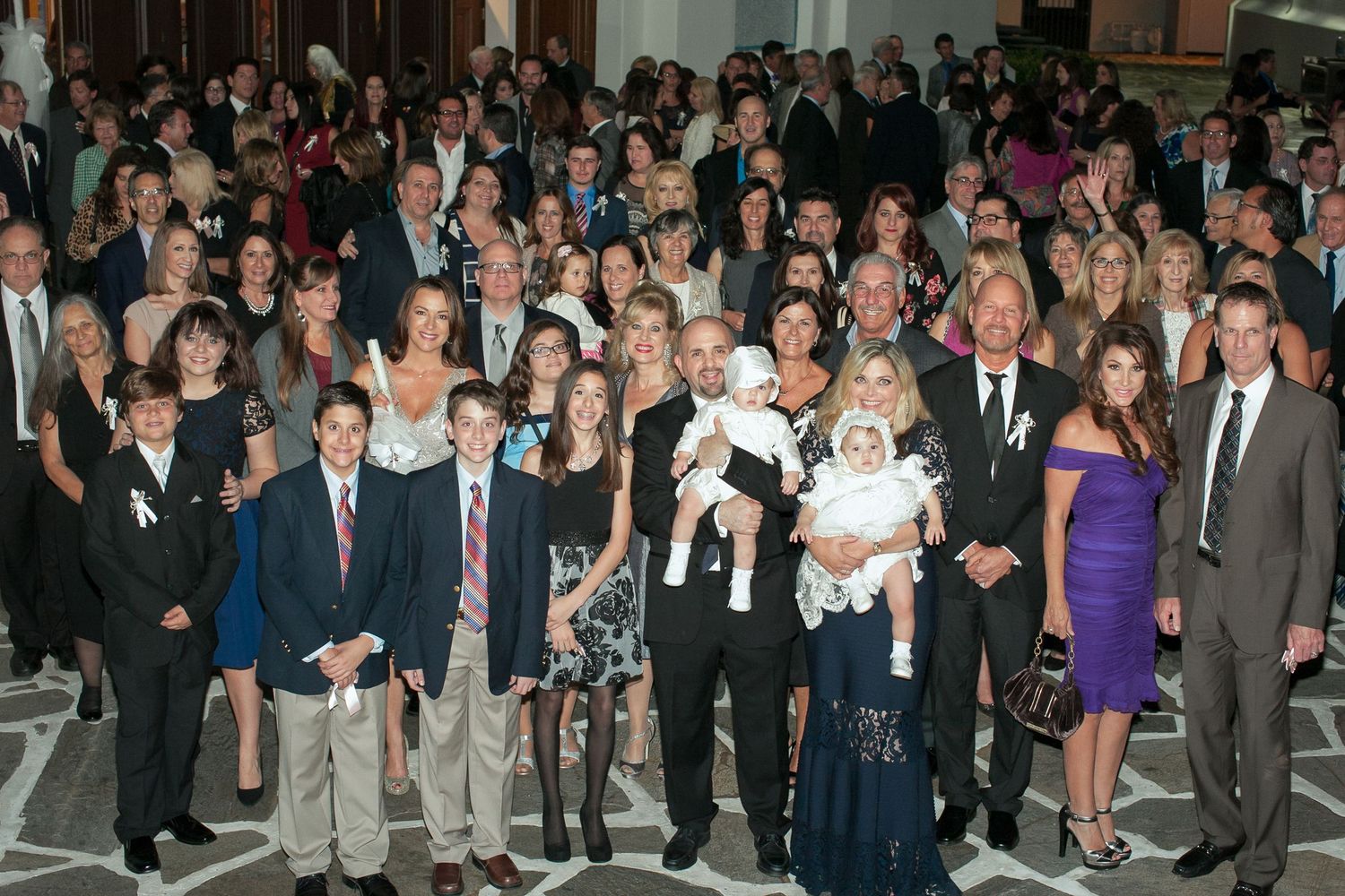 Large family group portrait at a formal wedding reception, with guests dressed in elegant attire posing together.