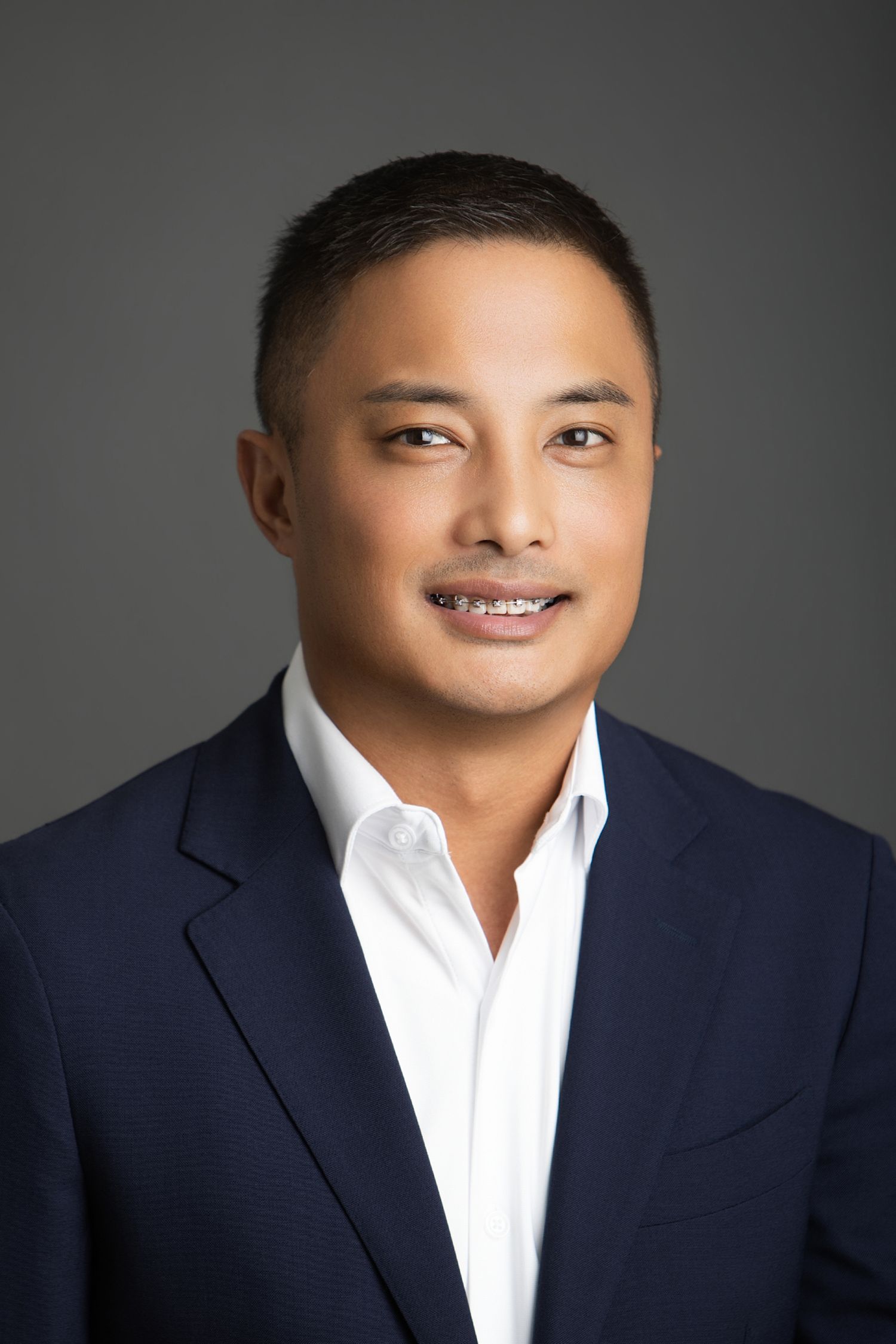 Professional headshot of a smiling man in a navy blazer and white shirt against a gray background.