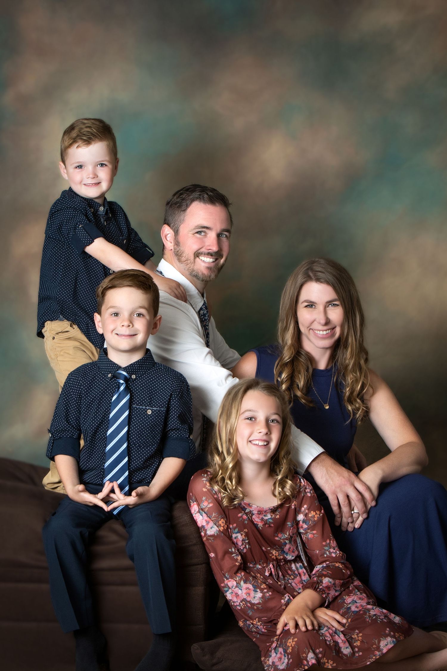 Professional family portrait of parents with three children posed together against a studio backdrop.