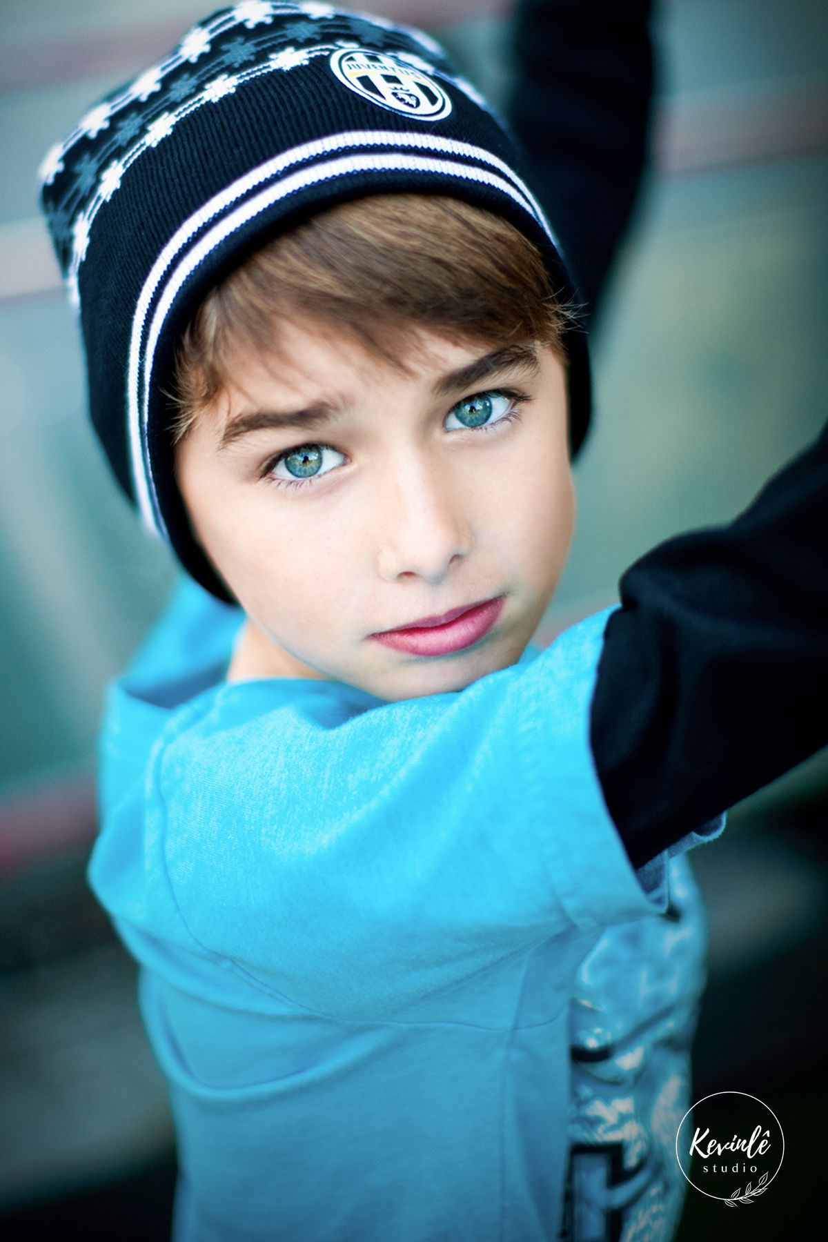 Blue-eyed child in winter beanie hat looking up in colorful outdoor portrait photo.