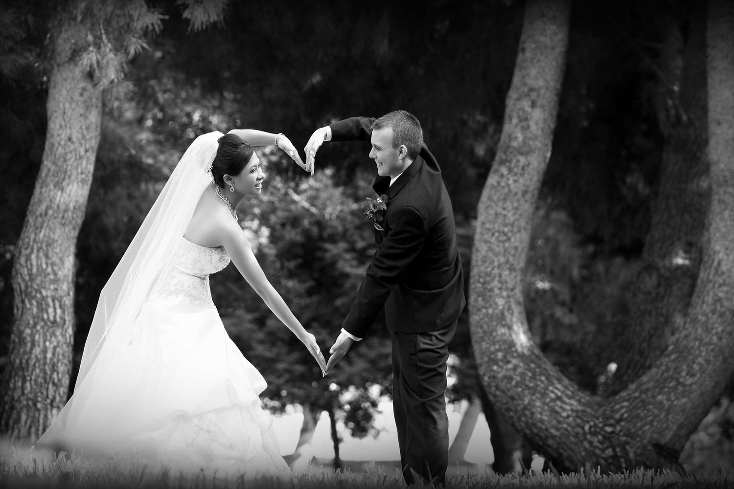 Black and white photo of a bride and groom holding hands among trees during an outdoor wedding ceremony.