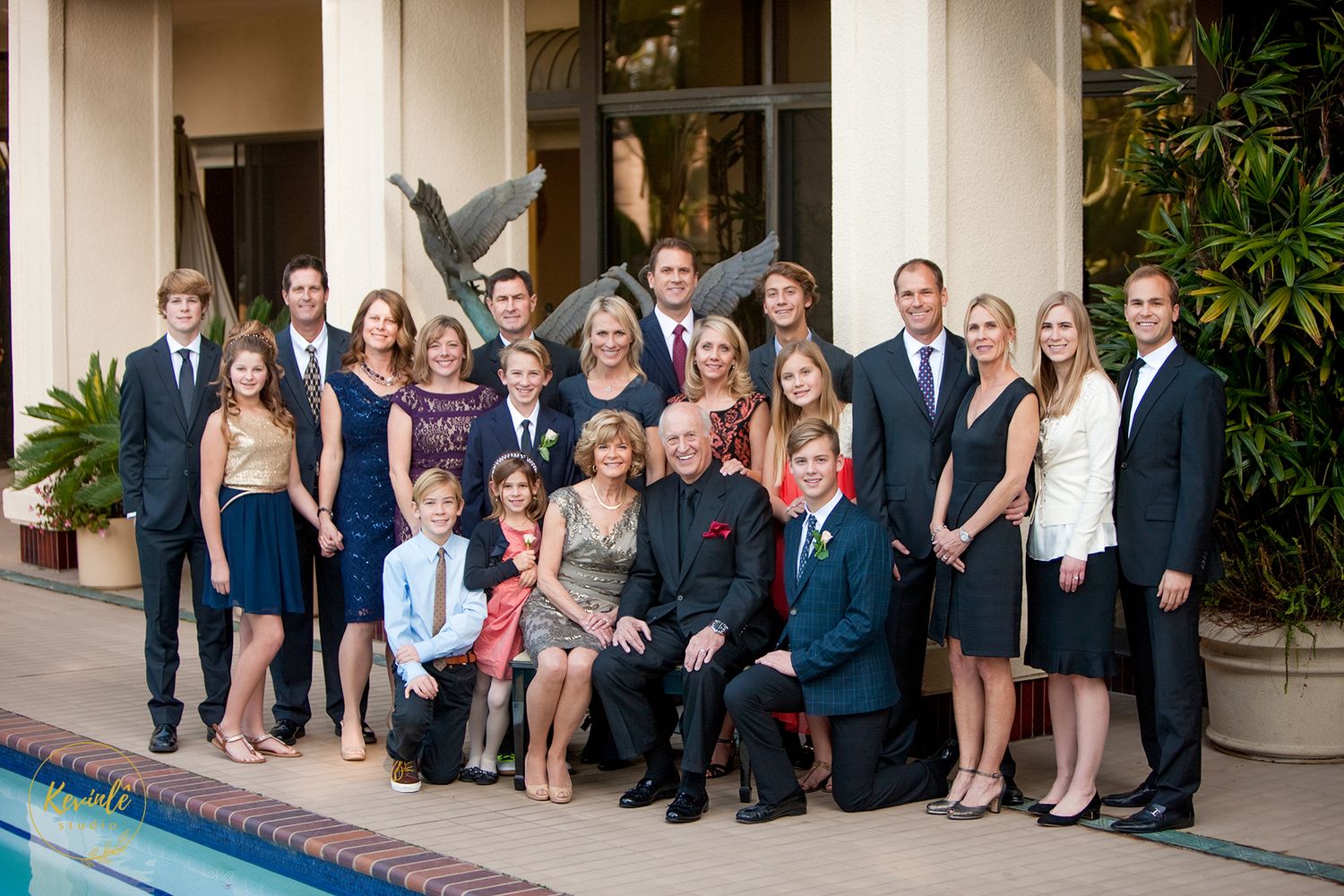 Large extended family group portrait posed outdoors near a pool at a formal evening event.