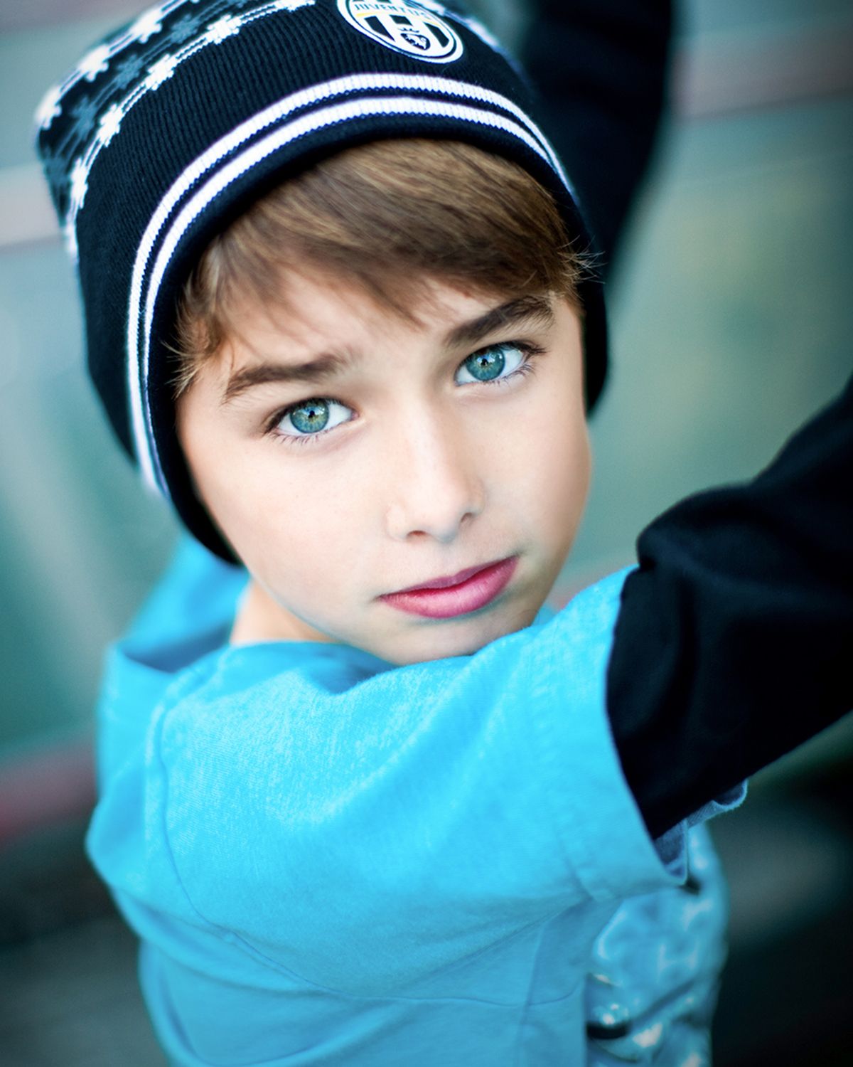 Young boy with striking blue eyes wearing a black beanie hat and blue shirt.