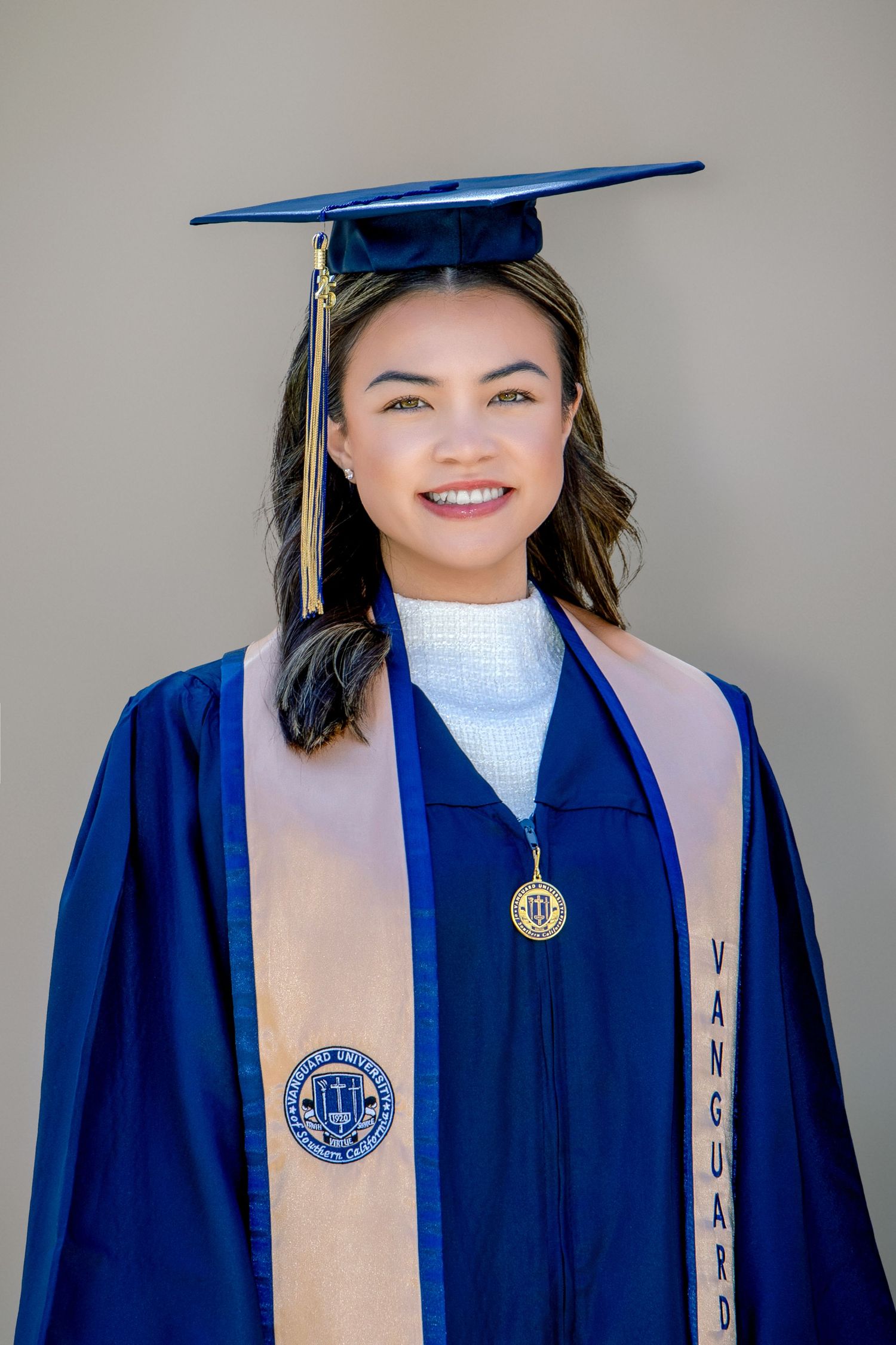 Smiling graduate in blue cap and gown with Vanguard University stole poses for a portrait photo.