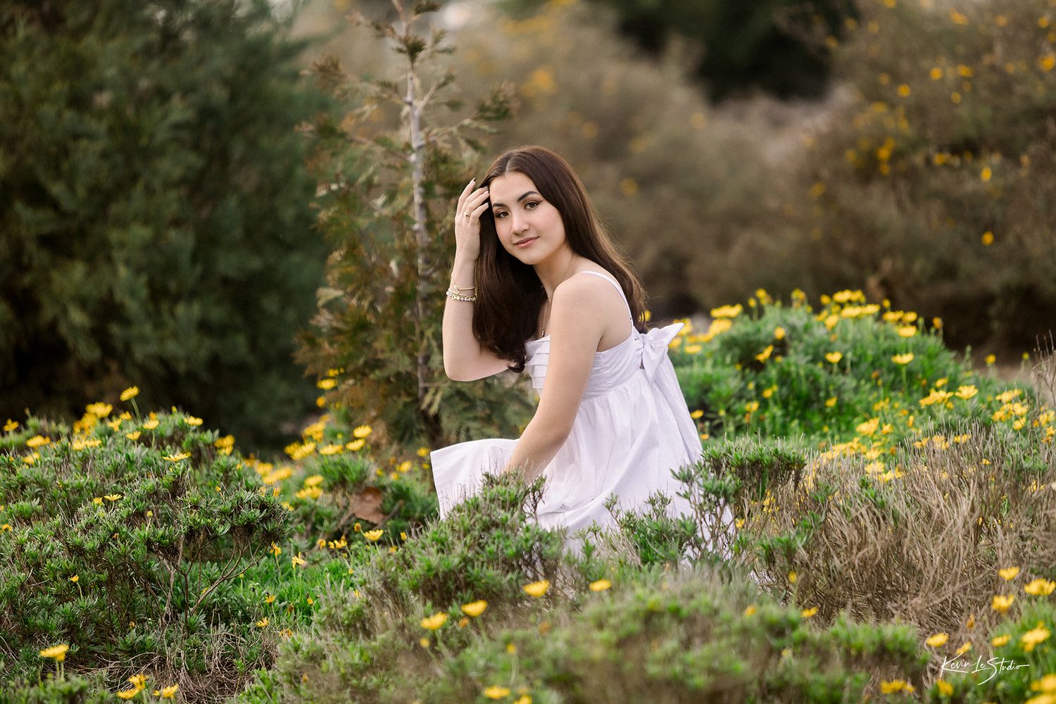 Young woman in white dress sits among yellow wildflowers in a lush garden setting.