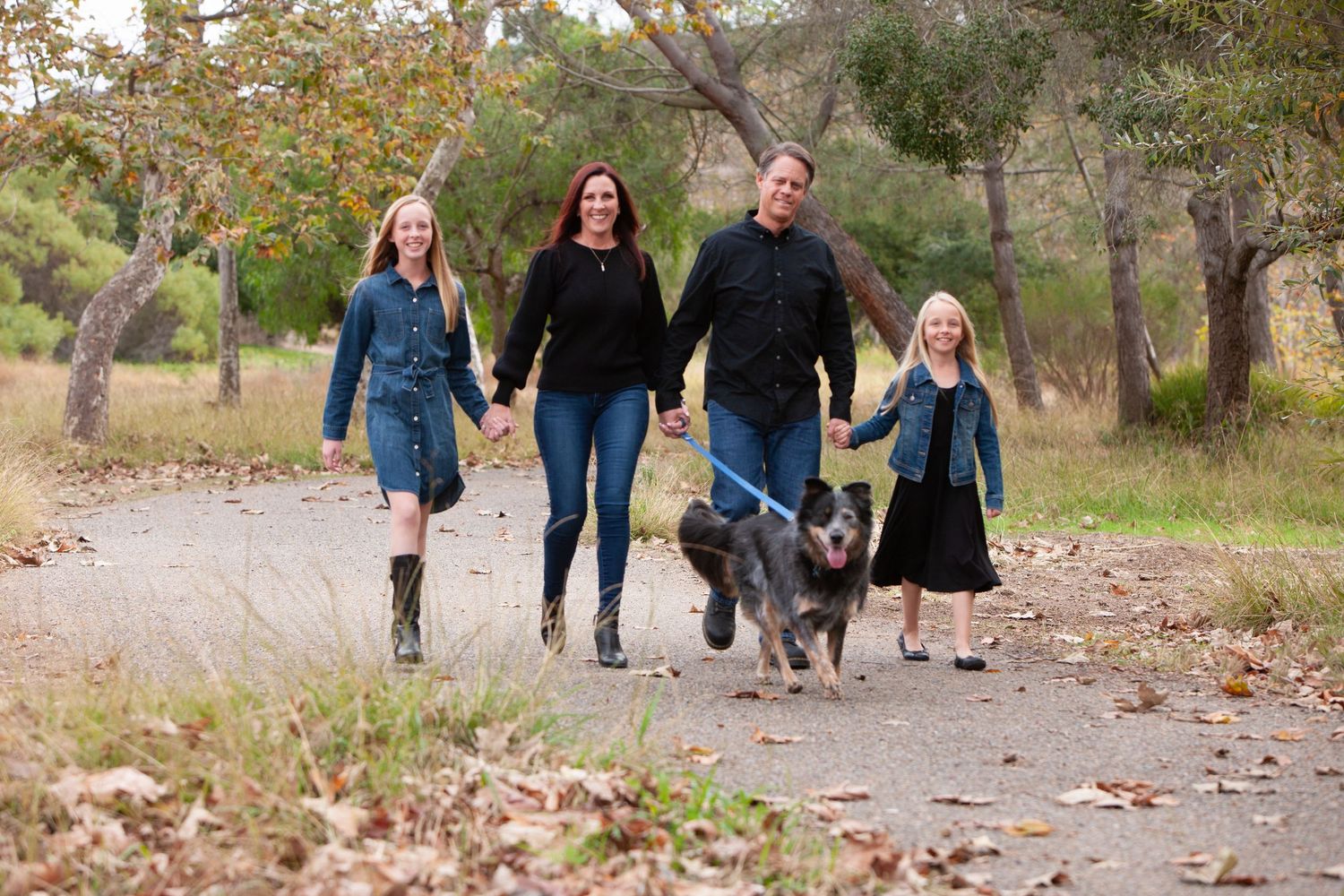 Family of four walking dog together on a scenic autumn park pathway.