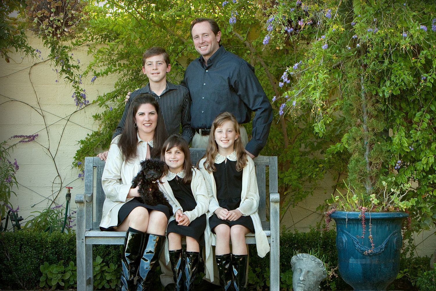Family of five posing on a garden bench with lush greenery, parents and three children dressed in coordinating outfits.