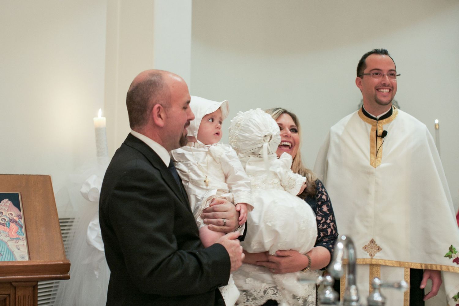 Family with baby in christening gown with priest during baptism ceremony in church.