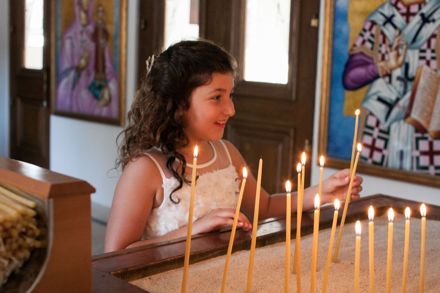Young girl in white dress lighting candles in an Orthodox church during a religious ceremony.