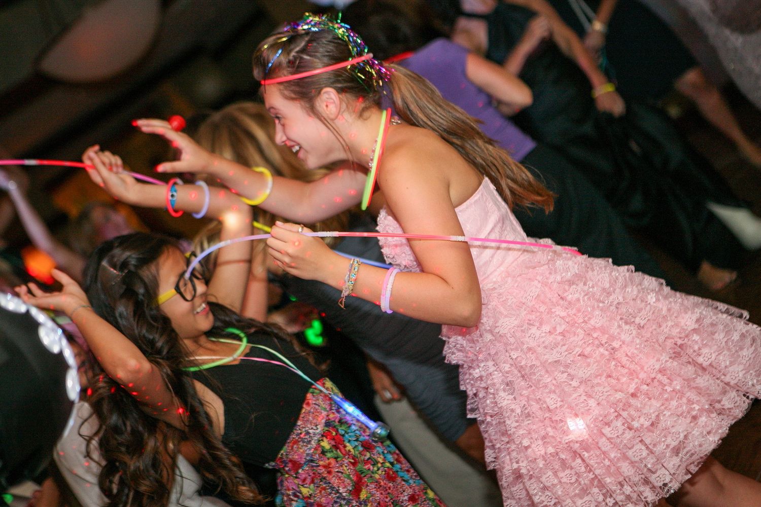 Young girls in colorful party dresses dancing and celebrating at a festive indoor party event.
