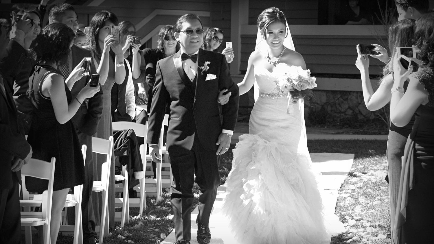 Black and white wedding photo of bride and groom walking down the aisle while guests celebrate.