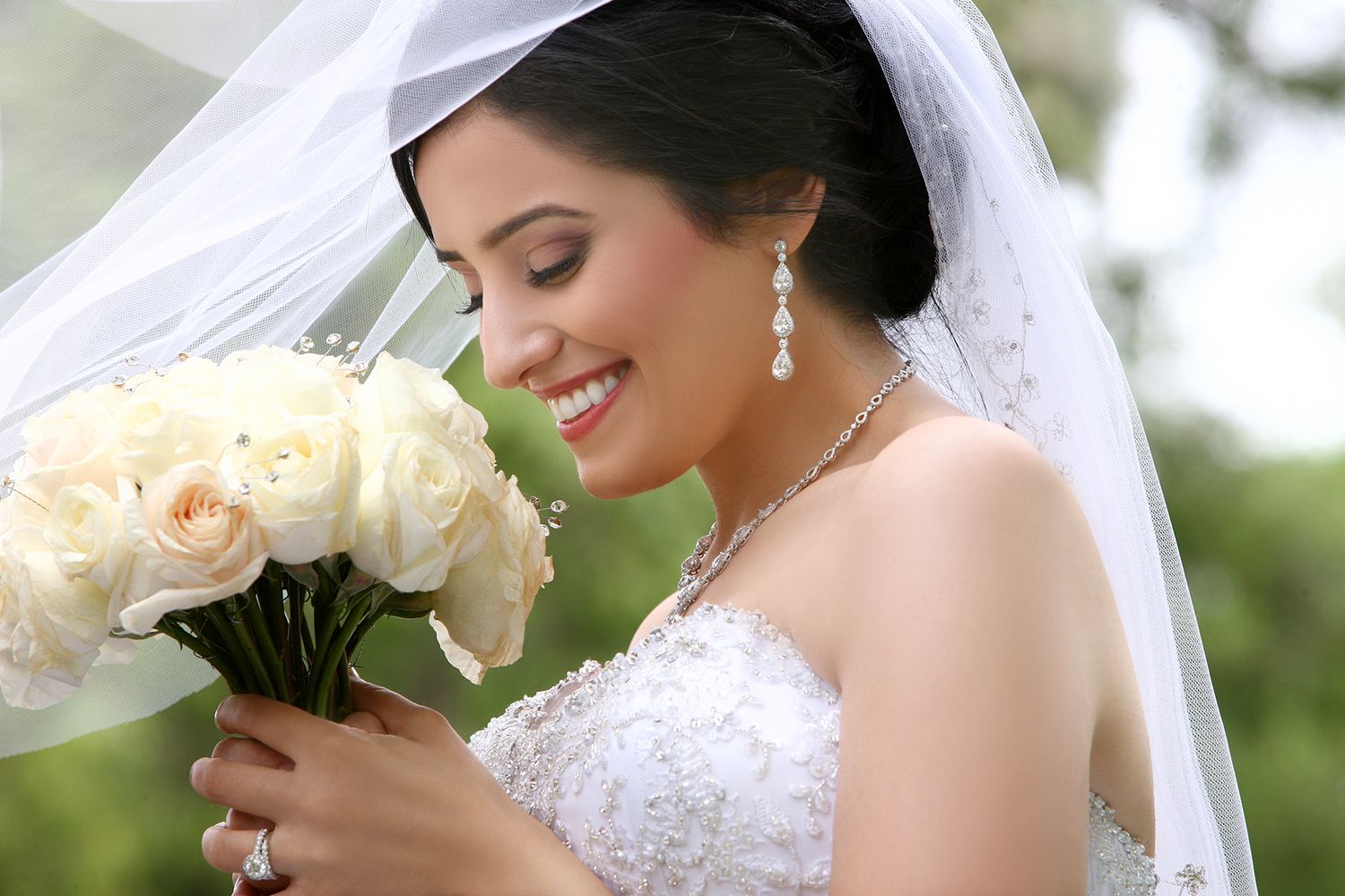 Beautiful bride smiling while holding a bouquet of white roses on wedding day.