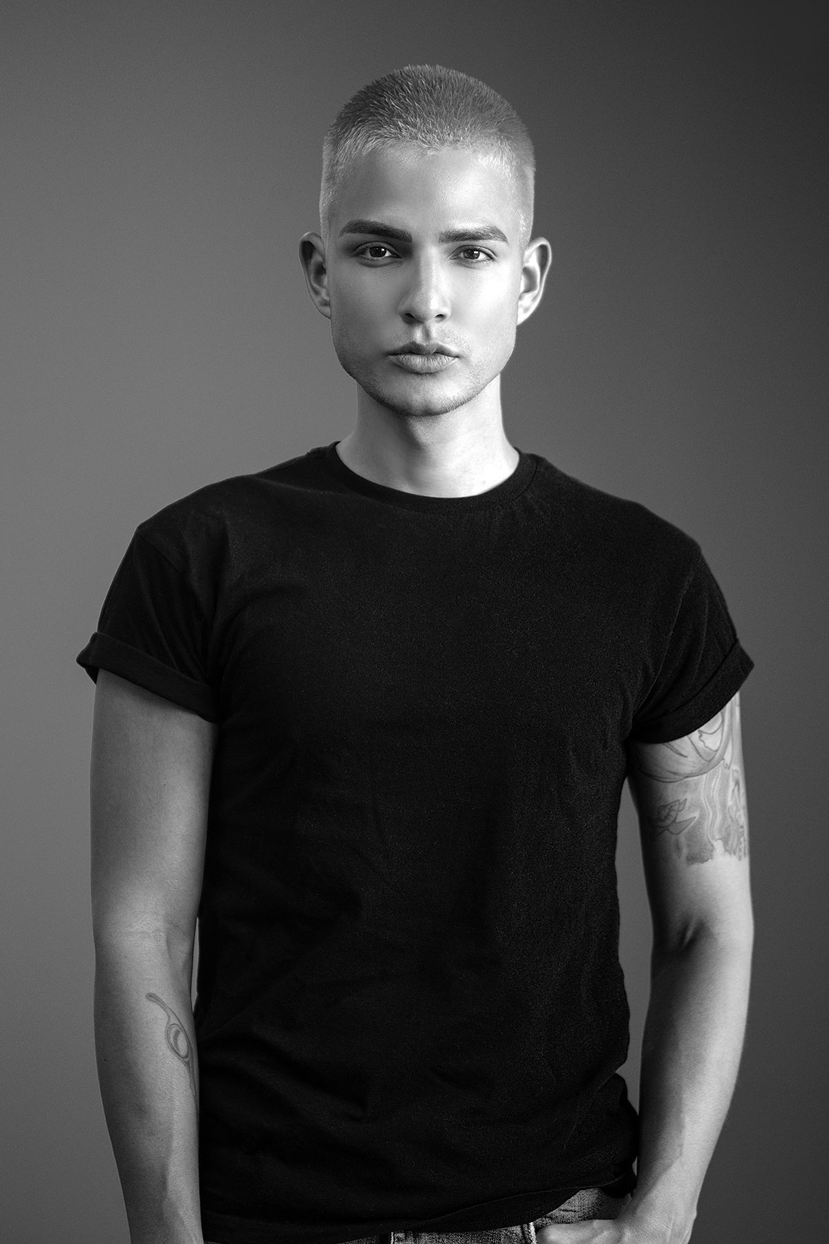 Tattooed young man with buzz cut in black t-shirt poses in black and white studio portrait.