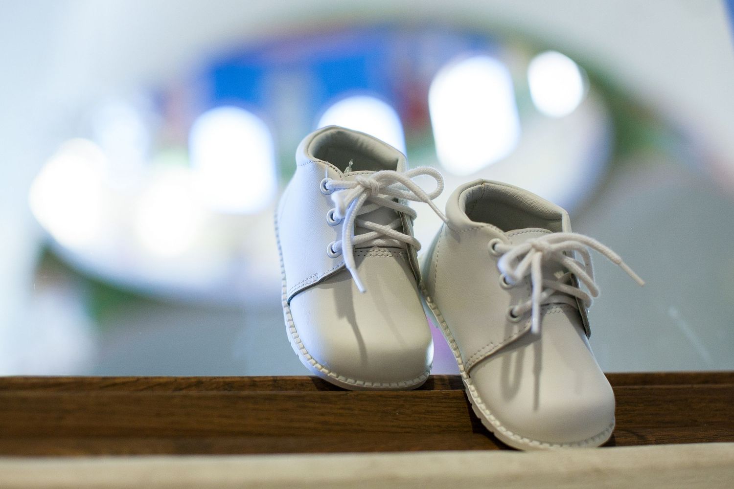 Tiny white baby shoes with laces displayed on a wooden surface with a soft blurred background.