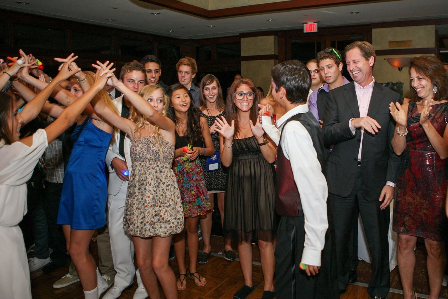 Teenagers dancing at a formal party event, gathered in a circle on a dance floor in elegant attire.