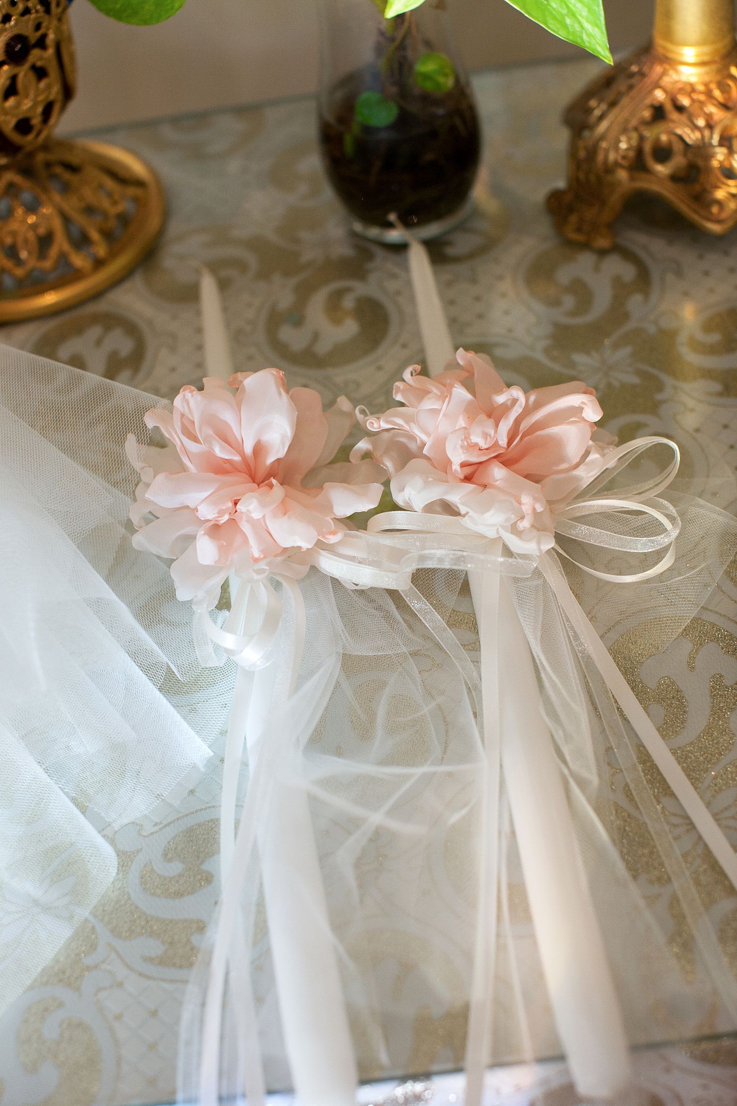 Two elegant white candles adorned with pink silk flowers and white tulle ribbons on a decorative table.